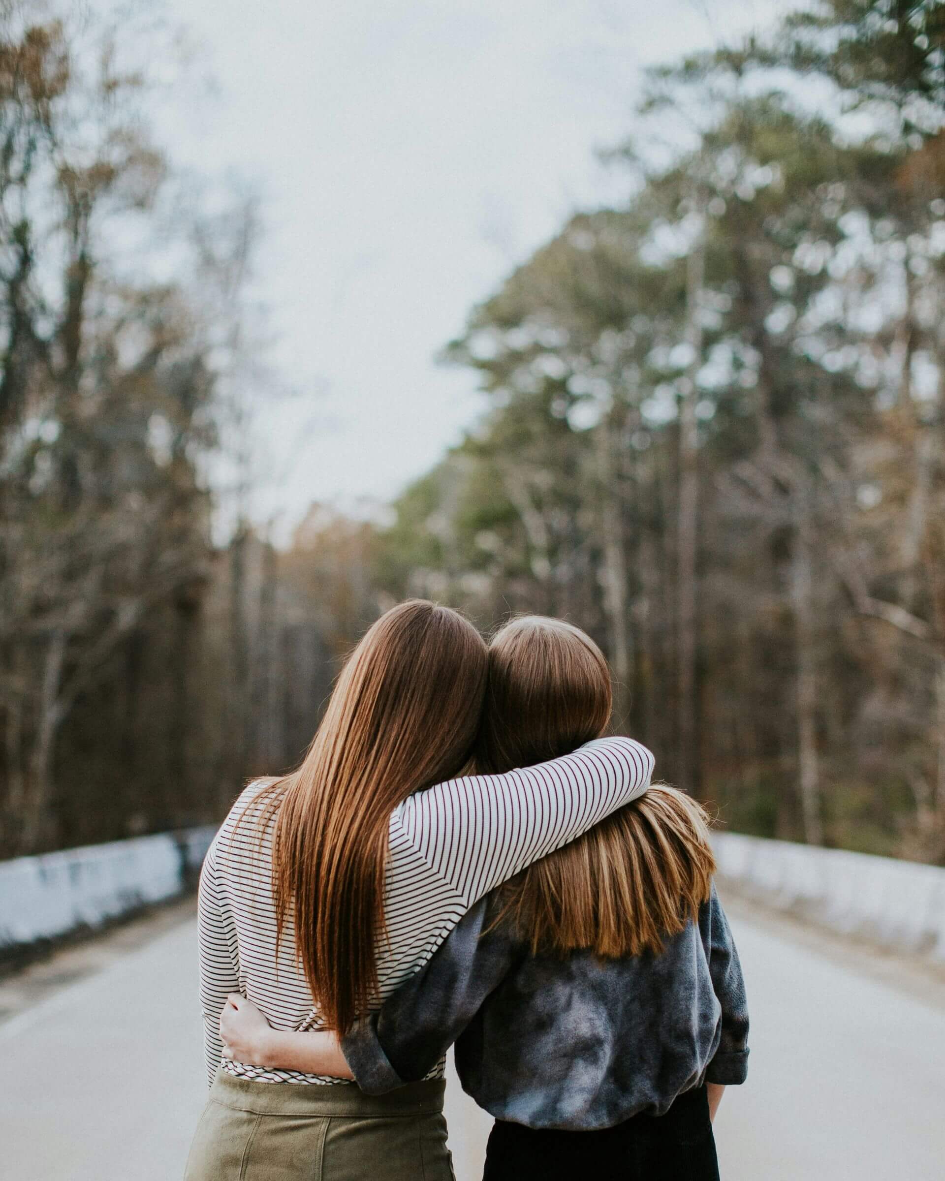 Two girls embracing each other on a forest road.